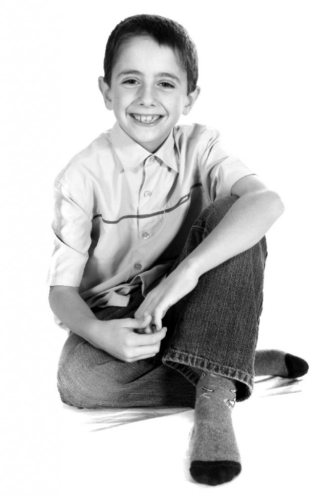 Black and white studio portrait of a boy sitting cross-legged and laughing